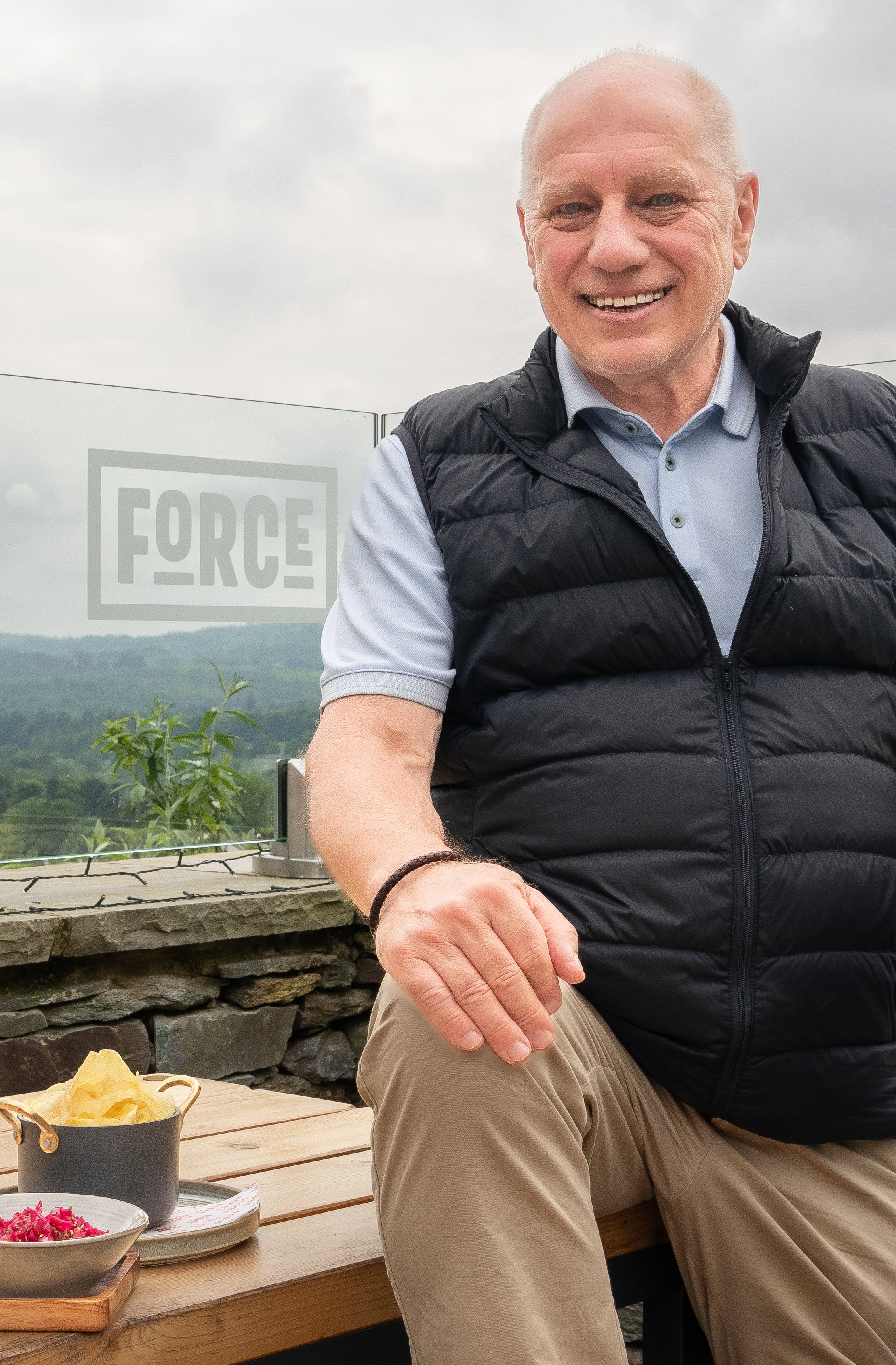 Man sitting at a table with scenic view, holding a walking stick